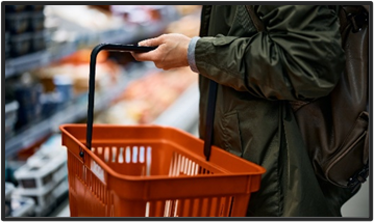 Close up of a person carrying a basket in a grocery store.